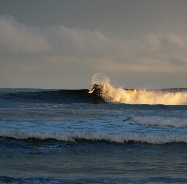 Surfing performing a snap with spray, early morning sunshine lighting uo the white water