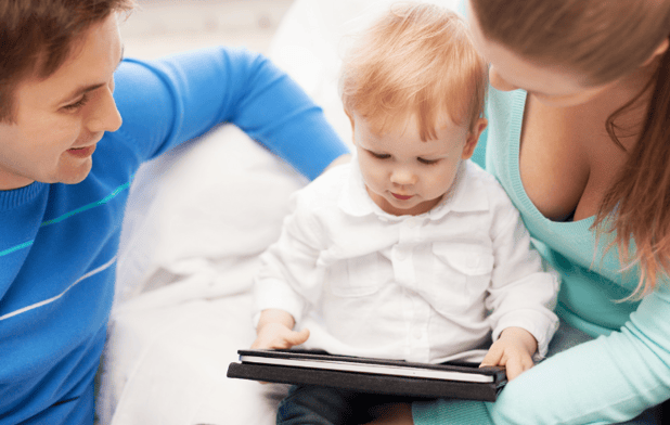 Pareja de padres jóvenes que esán con  un niño de dos años viendo una tablet.