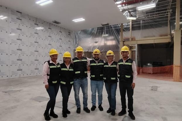 a group of men in hard hats and safety vests standing in a warehouse