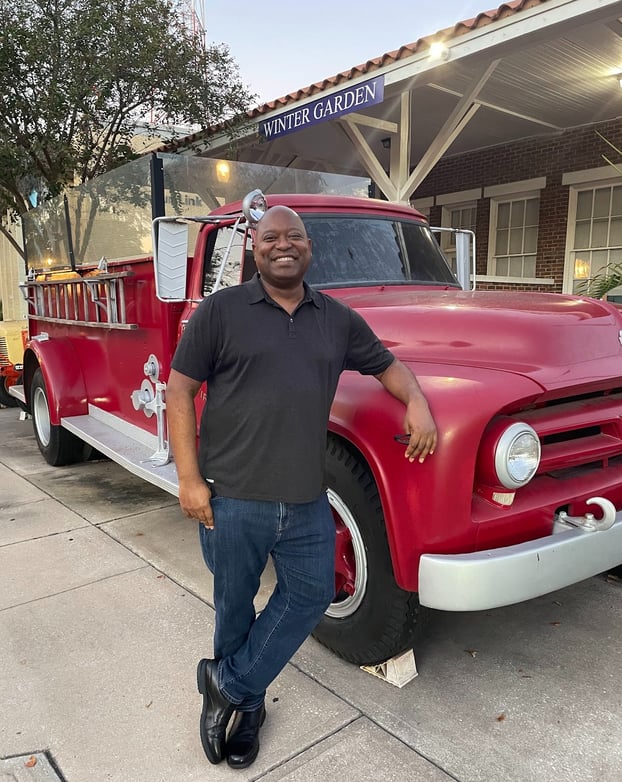 Photo of attractive dark skinned male leaning against a vintage red fire truck