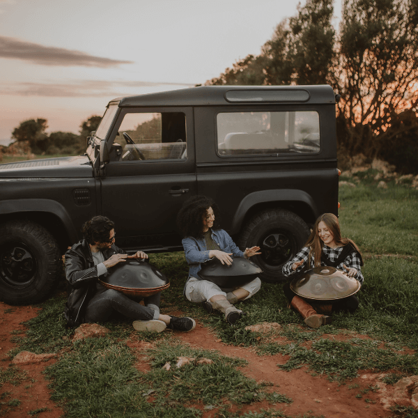 Three musICIAn playing Sew Handpan on the nature close to a jeep