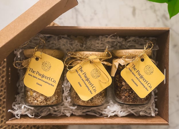 A gift box containing three glass jars of Panjeeri flavours: chocolate, dates, and classic