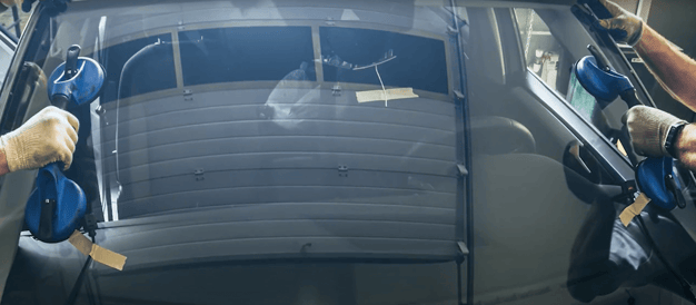 two workers hold windshield with suction cups