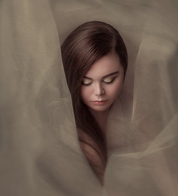 Creative portrait of a young woman wrapped in sheer tulle, creating an ethereal, dreamy effect.