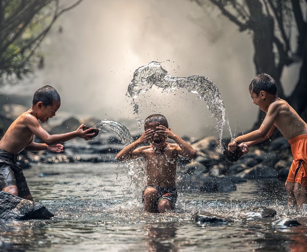 three boys playing in a stream of water