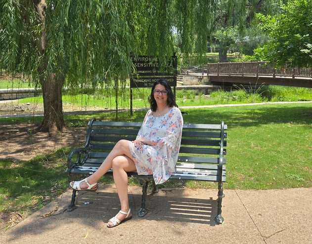 Angela sitting on a bench in the park under a tree.