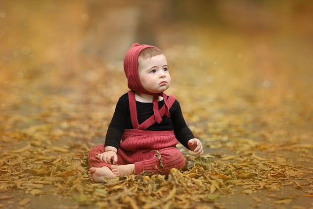 a baby girl sitting on a leaf covered ground