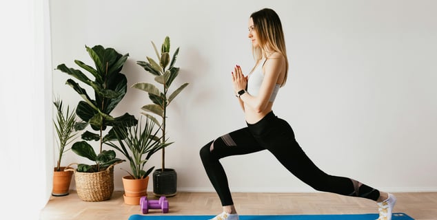 Mujer realizando una postura de zancada con las manos juntas durante una clase de pilates online ofrecida por Yarkeey.