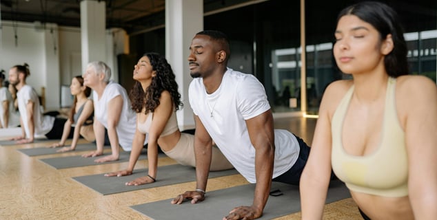 Grupo diverso de personas de varias edades practicando yoga o pilates juntos en una clase presencial, ilustrando las dinámica