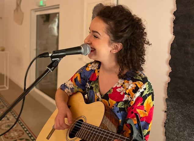 Une femme musicienne qui joue de la guitare et qui chante dans un micro sur pied