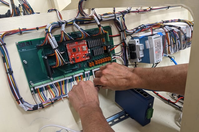 two hands holding a wiring harness with a rainbow of wires leading to a green circuit board