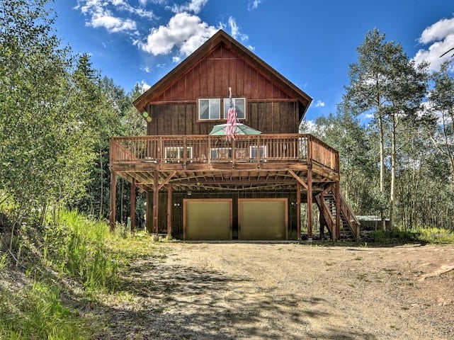 Rustic mountain cabin with a large elevated deck and two-car garage, surrounded by aspen trees.