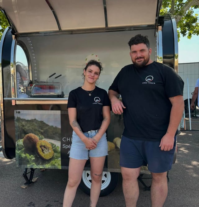 a man and woman standing in front of a food "Chez Tosca" truck