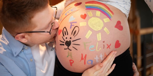 werdender Vater küsst bemalten Babybauch seiner schwangeren Frau