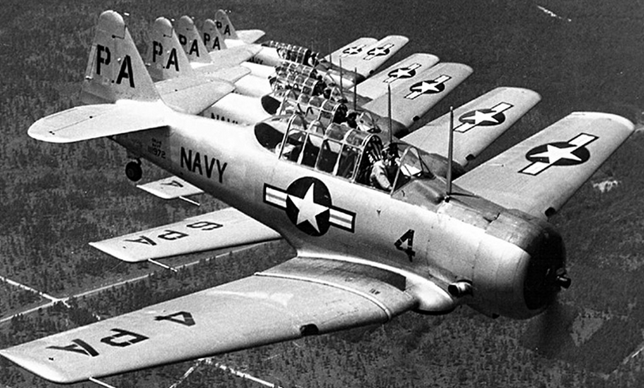 Group of six T-6 Texan aircraft flying in formation, US Navy paint scheme