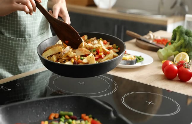 Person stirring roasted vegetables in a pan in a modern kitchen.