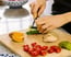 A person slicing a cucumber on a cutting board with various fresh ingredients.