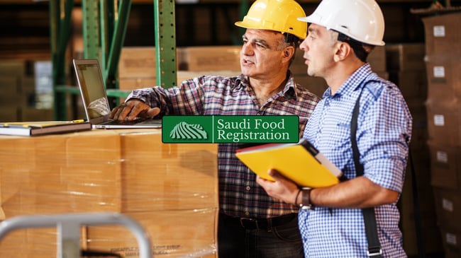 warehouse workers reviewing shipment documents on a laptop, representing customs clearance with Saudi Food Registration.