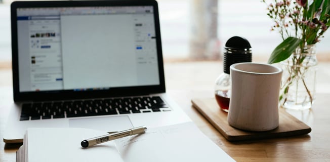 a laptop computer and a notebook with a pen and a cup of coffee