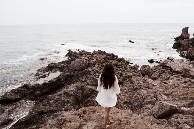 a woman in a white dress standing on a rocky beach