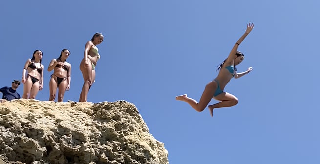 a woman jumping into the water from a cliff