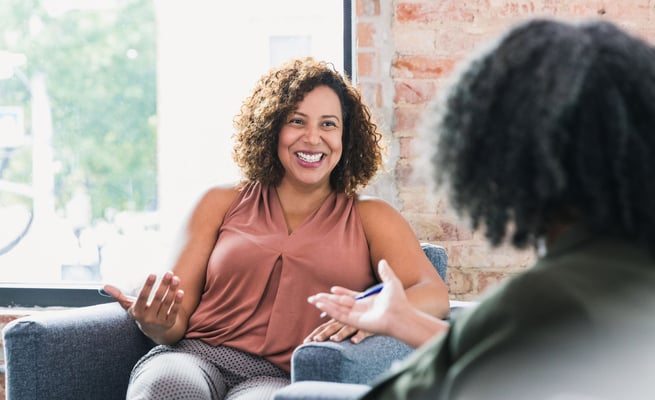 a woman sitting on a couch talking to another woman 