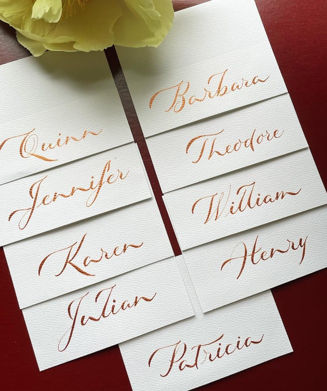 Beautiful calligraphy place cards in metallic bronze ink on white paper showcased on red background 