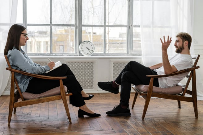 una psiquiatra entrevistando a un paciente sentados en sillas en una sala luminosa