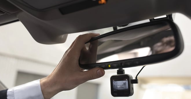 Dashcam debajo de un espejo retrovisor y la mano de un hombre acomodandola