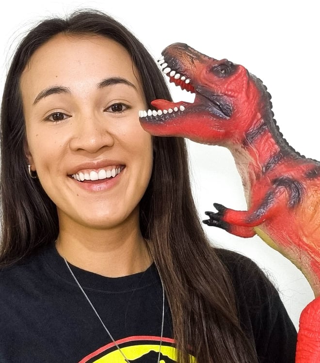 A half Chinese woman holding a dinosaur toy wearing a Jurassic Park t-shirt