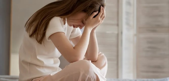 a woman sitting on a bed with her hands on her head