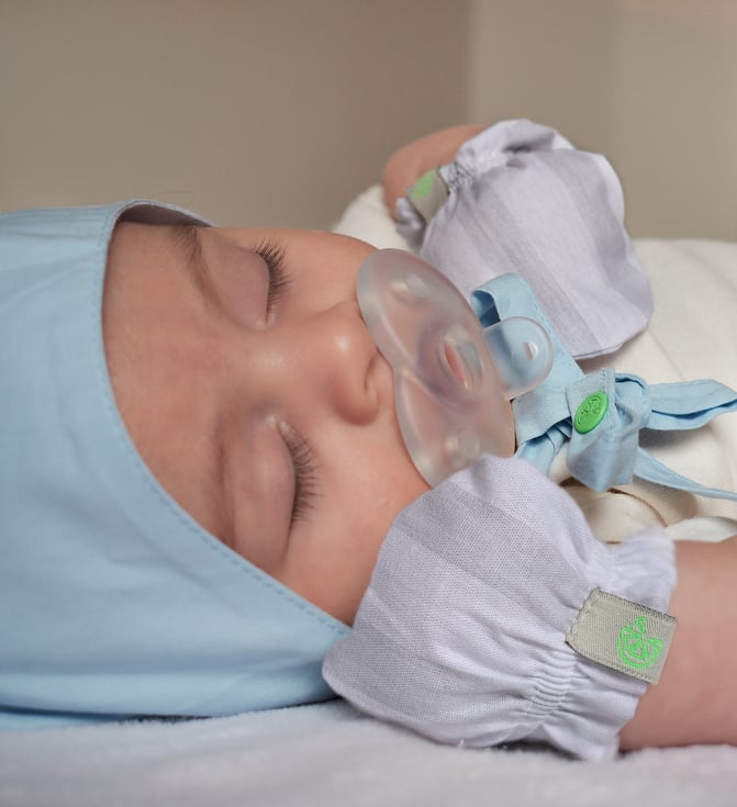 Bebê dormindo de luvas e touca.