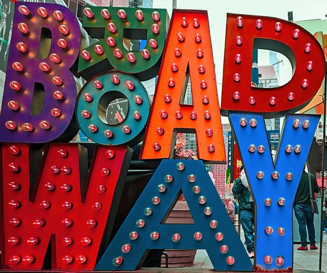 brightly colored "BROADWAY" sign with illuminated bulbs stands in Times Square, New York City