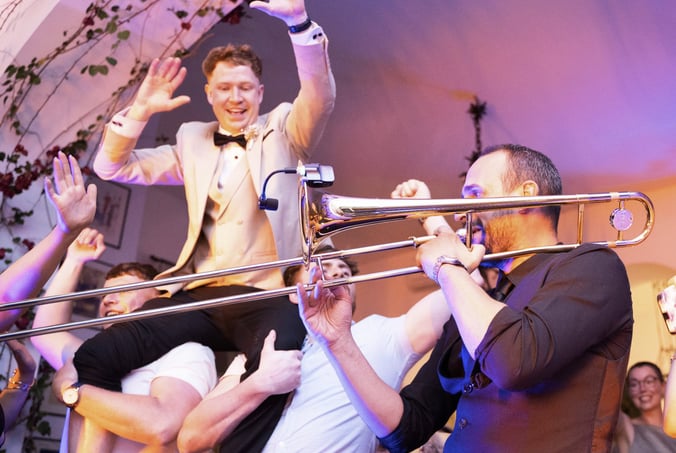 Groom lifted by friends on the dance floor while band plays live trombone