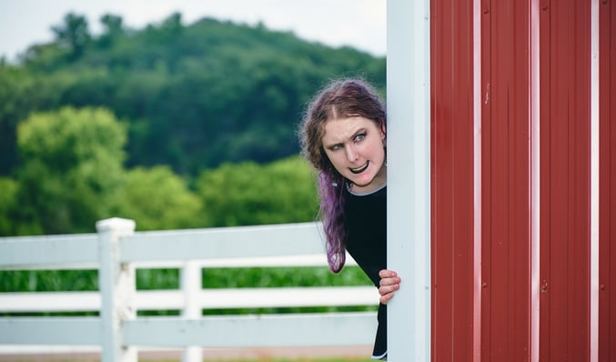 a girl with purple long hair looking out over a barn house with evil expression