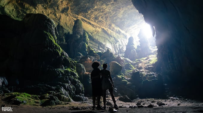a couple standing inside a Bat Cave in Vietnam, as light enters the cave