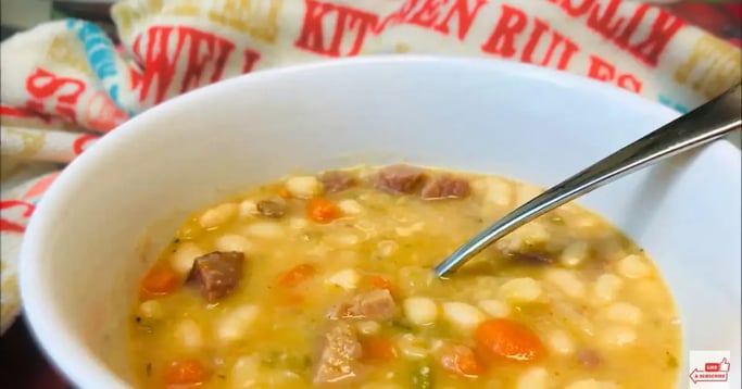White bowl of navy bean soup with spoon and kitchen towel in the background