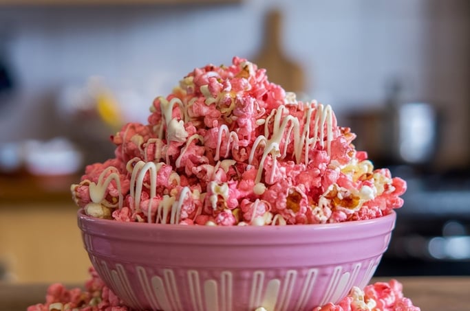 A vibrant bowl of pink-dyed popcorn mixed with white chocolate drizzle
