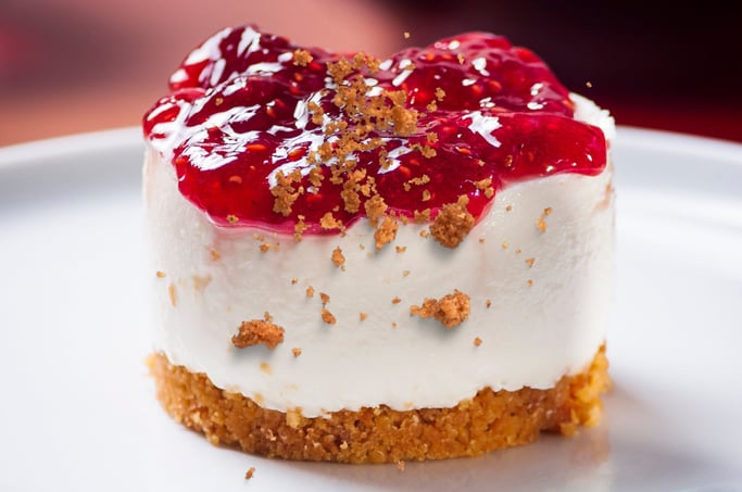 Mini cheesecake cups topped with fresh raspberries and a dusting of graham cracker crumbs