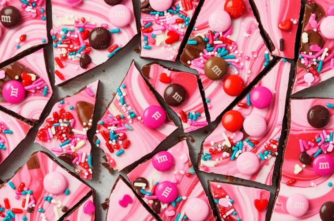 A colorful sheet of Valentine’s Day bark broken into irregular pieces, with pink swirls, M&M's, and
