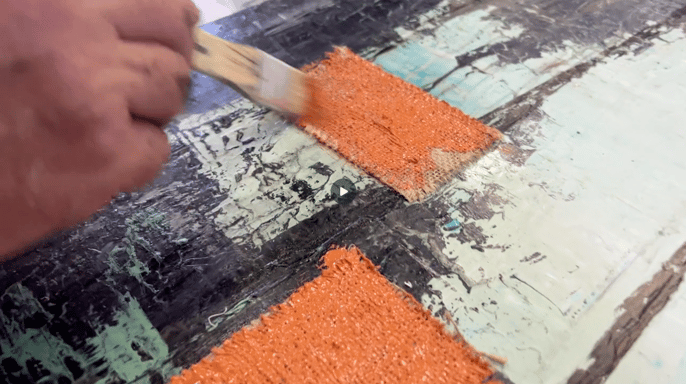 Martin Osner applying textured rust pigment to a layered mixed media artwork on board.
