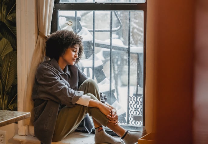 a depressed woman sitting on a window sill with her feet on the floor