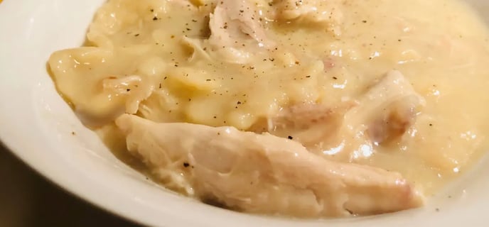 A bowl of old-fashioned Southern chicken and dumplings served in a white bowl with orange spray floral in the background.