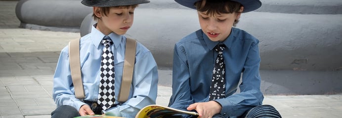 two boys sitting on a bench reading a book