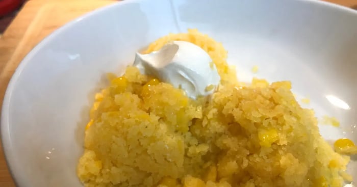 Mexican Corn Cake in white bowl with dollop of sour cream and corn kernals scattered in bowl.
