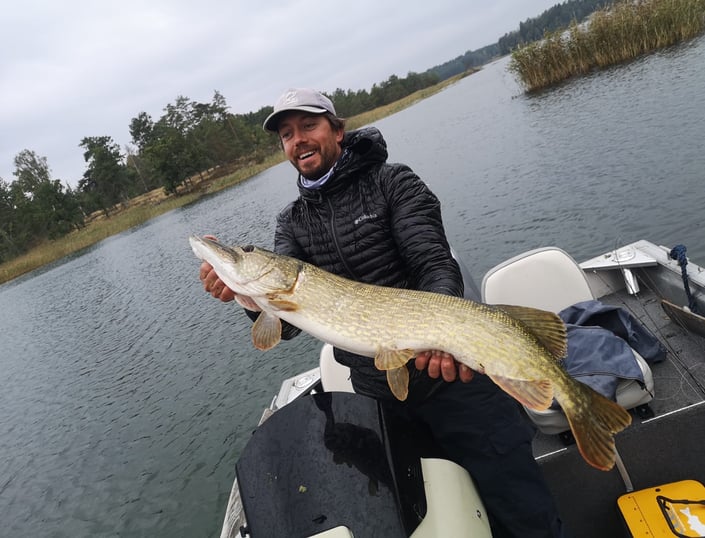 A man is on a boat, he is happy to have caught a big pike in Sweden.