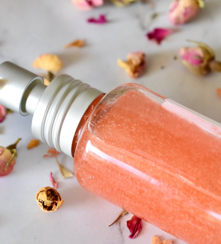 flacon de serum rose posé sur une table en marbre avec des pétales de rose