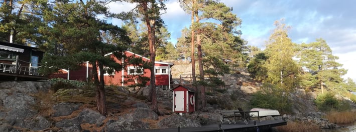 une maison rouge suédoise est au bord de l'eau , il y a des arbres autour de la maison.