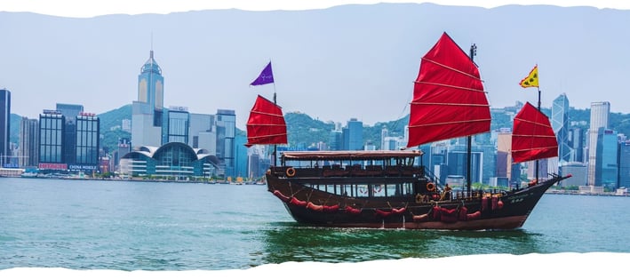 Foto de fundo da página com barco local navegando pela baía, tendo a cidade de Hong Kong ao fundo envolta em névoa