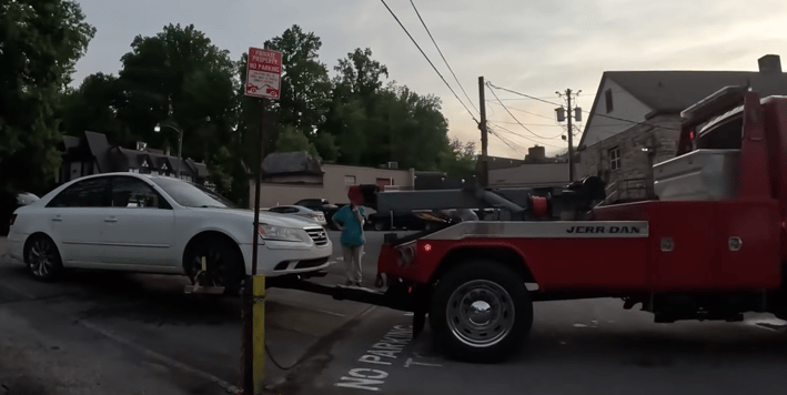 Red to truck hooking a white automobile, readying it to be towed from a parking lot.